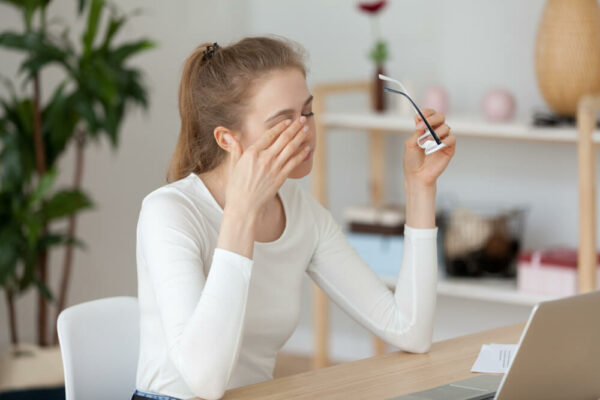 Young woman sitting at the desk in office at workplace took off eyeglasses massaging her eyes.