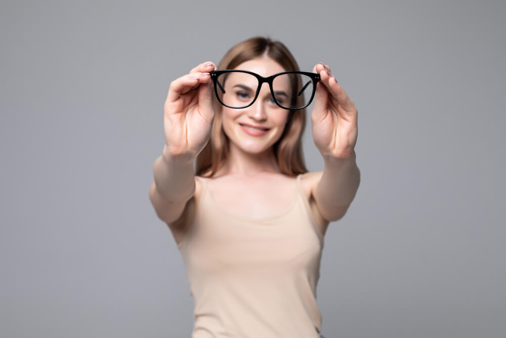 Glasses - optician showing eyewear. Closeup of glasses, with glasses and frame in focus. Woman optometrist on white background.