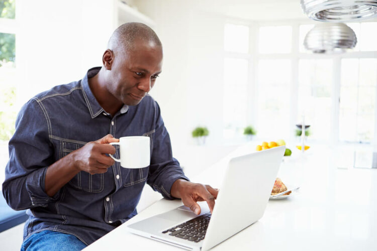 Man drinking coffee at home looking at laptop